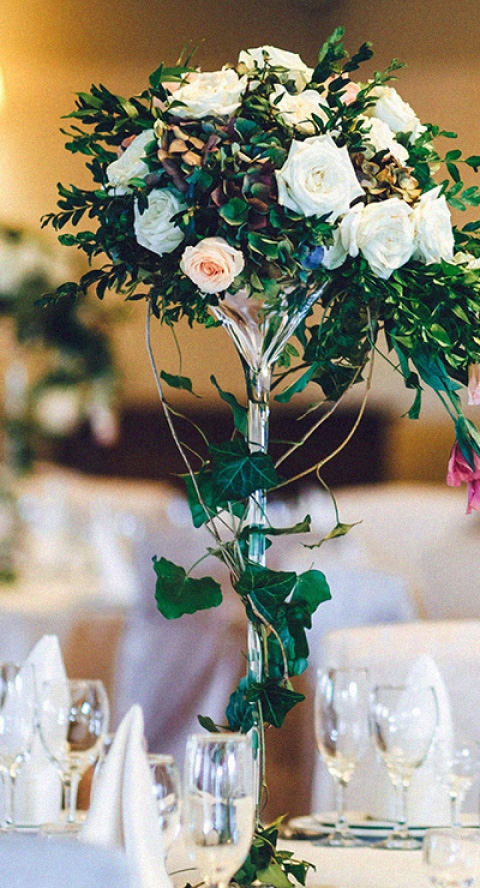 Nice flowers in a pretty glass vase on a nicely decorated table and tablecloth with glassware.