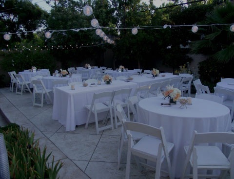 White tables and chairs with white tablecloths and flowers on top arranged for a party.