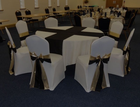 Circle tables with white tablecloths and black table runners with white chairs with black chair sashes.