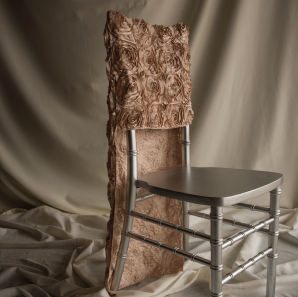 Champagne colored rosette chair cover on a silver colored Chiavari chair in front of a white back drop.