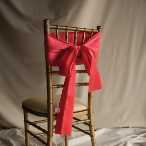Back of a coral colored chair sash tied into a bow on a silver chair.