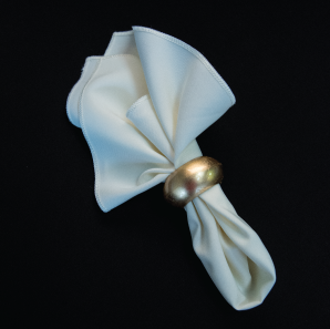 Close up of an ivory colored napkin in a gold napkin ring.