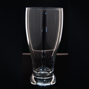 Close up of a pilsner glass in front of a black backdrop.