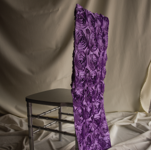 Purple rosette chair cover on a silver colored Chiavari chair in front of a white back drop.