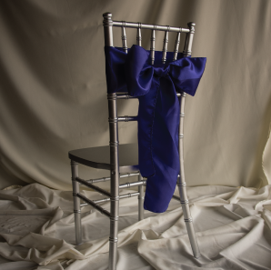 Back of a royal blue chair sash tied into a bow on a silver chair.