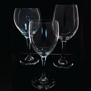 Close up of three small wine glasses in front of a black backdrop.